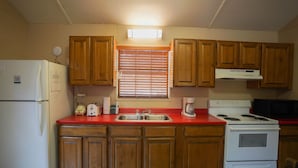 A kitchen with wooden cabinets, a white refrigerator, a stove, and a sink. - Frio Country Resort - Within walking distance to the Frio River! (Concan)