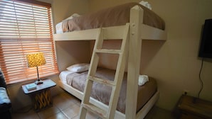 A bunk bed room with a ladder, a bedside table with a lamp, and a window with blinds. - Frio Country Resort - Within walking distance to the Frio River! (Concan)