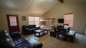 A living room with a sofa, a coffee table, a bunk bed, a TV, and a dining table. - Frio Country Resort - Within walking distance to the Frio River! (Concan)