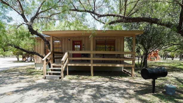 A wooden cabin with a porch, a staircase, and a mailbox. - Frio Country Resort - Within walking distance to the Frio River! (Concan)