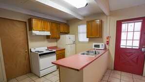 A compact kitchen with wooden cabinets, a white refrigerator, a microwave, and a red door. - Frio Country Resort - Within walking distance to the Frio River! (Concan)