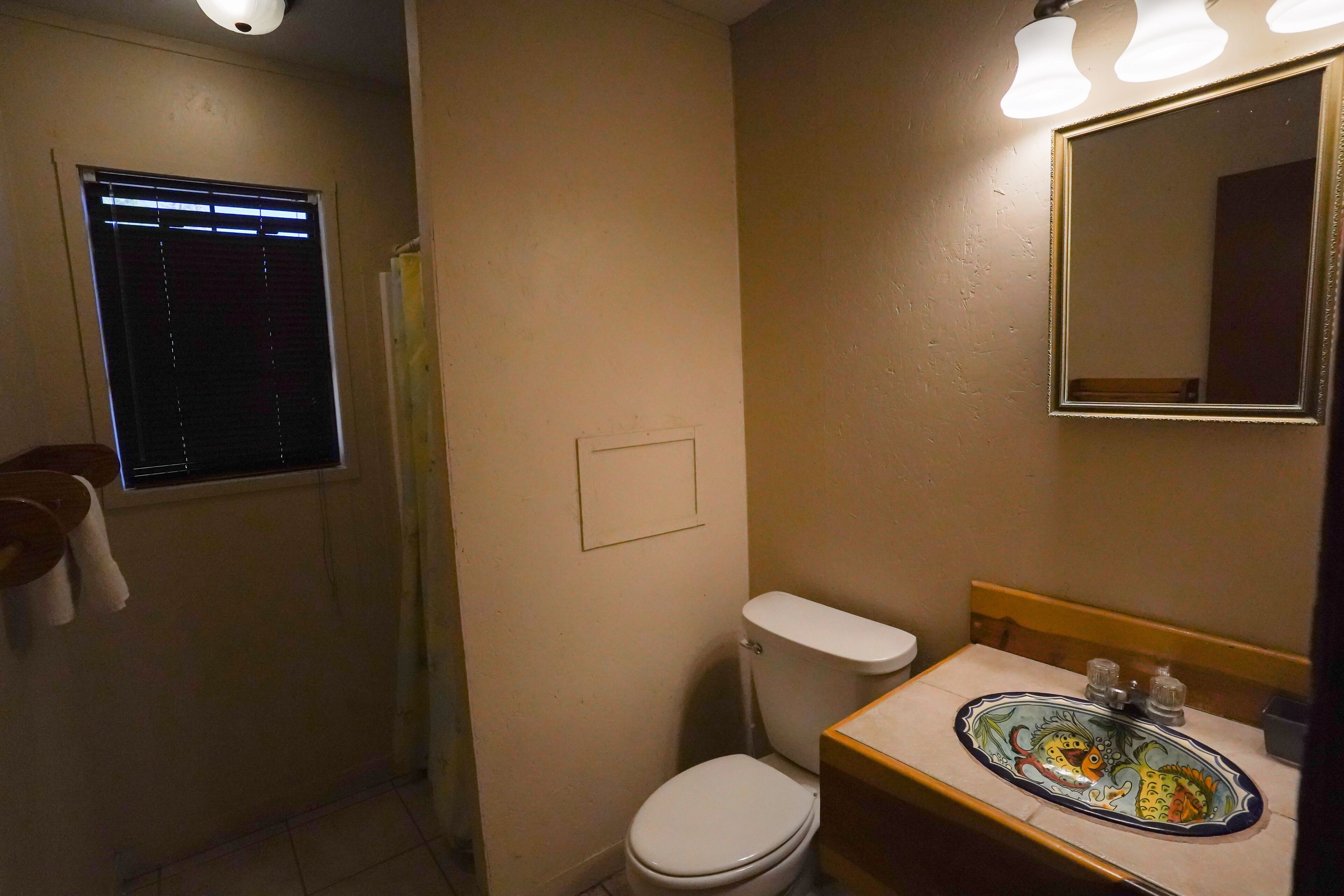 A bathroom with a toilet, sink, mirror, and window with blinds.