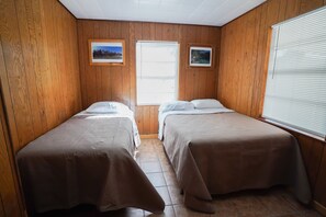 Une chambre avec deux lits, des murs en bois et deux tableaux encadrés accrochés au mur.