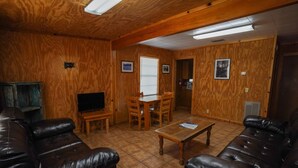 Ein Wohnzimmer mit Holzpaneelen, einem schwarzen Ledersofa, einem Holztisch und einem Fernseher auf einem Schrank.