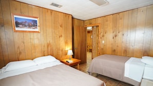 Ein Hotelzimmer mit zwei Betten, Holzwänden, einem gerahmten Bild an der Wand und einem Nachttisch mit Lampe.
