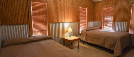 A room with two beds, wooden paneling on the walls, a small table with a lamp, and a radiator.