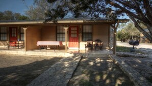 A rustic cabin with a covered porch, a red door, and a table with chairs. - Frio Country Resort - Within walking distance to the Frio River! (Concan)