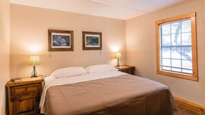 A bedroom with a bed, two bedside lamps, a window, and two framed pictures on the wall. - Frio Country Resort - Within walking distance to the Frio River! (Concan)