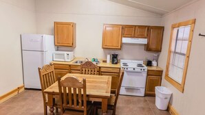 A compact kitchen with wooden cabinets, a white refrigerator, a microwave, a stove, and a dining table with chairs. - Frio Country Resort - Within walking distance to the Frio River! (Concan)