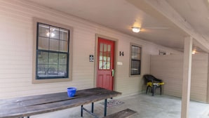 A covered outdoor area with a red door, numbered room 14, a bench, and a plastic chair. - Frio Country Resort - Within walking distance to the Frio River! (Concan)