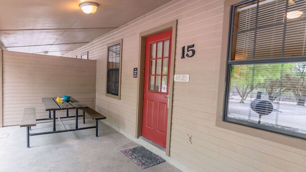 A hallway with a red door, numbered 15, and a bench with a doormat. - Frio Country Resort - Within walking distance to the Frio River! (Concan)