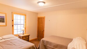 A room with two beds, a wooden door, a window with blinds, and a nightstand with a lamp. - Frio Country Resort - Within walking distance to the Frio River! (Concan)