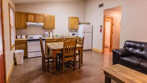 A compact kitchen with wooden cabinets, a dining table, and a black leather couch. - Frio Country Resort - Within walking distance to the Frio River! (Concan)