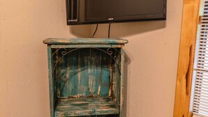 A teal, distressed wooden shelf unit with a flat-screen TV mounted above it, positioned against a wall with a window on the right. - Frio Country Resort - Within walking distance to the Frio River! (Concan)
