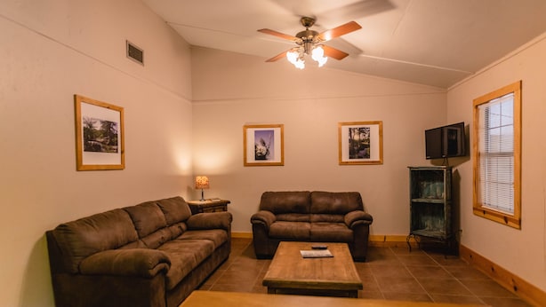 A living room with a brown leather sofa, a wooden coffee table, and two framed pictures on the wall. - Frio Country Resort - Within walking distance to the Frio River! (Concan)