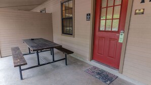 A covered outdoor area with a wooden bench and a red door. - Frio Country Resort - Within walking distance to the Frio River! (Concan)