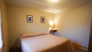 Un dormitorio con una cama, una mesita de noche con lámpara y dos cuadros enmarcados en la pared.