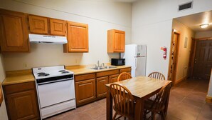 Una cocina funcional con armarios de madera, estufa blanca, microondas y refrigerador. Hay una mesa de comedor de madera con sillas.