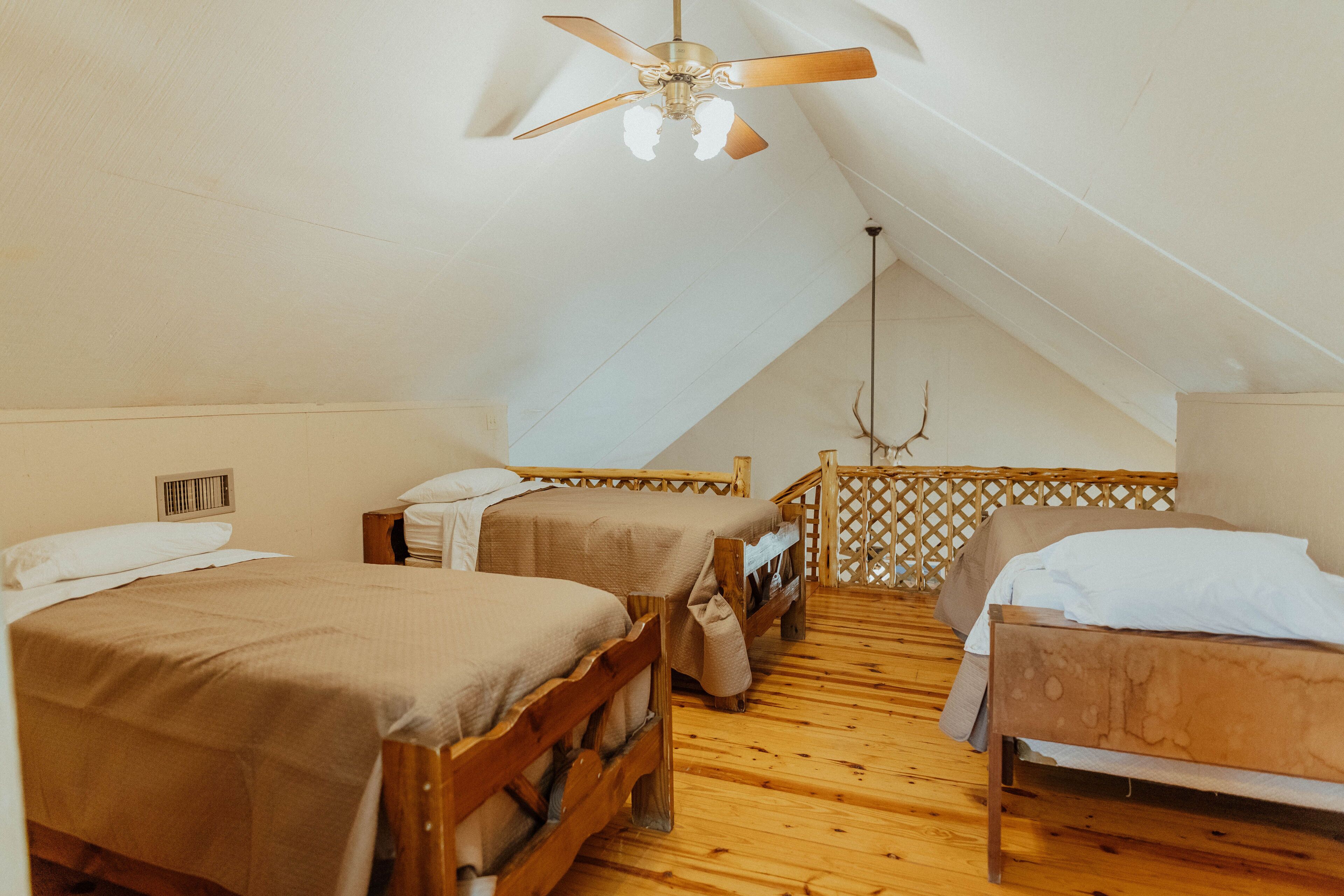 Une chambre avec deux lits en bois, un ventilateur de plafond et un plancher en bois.