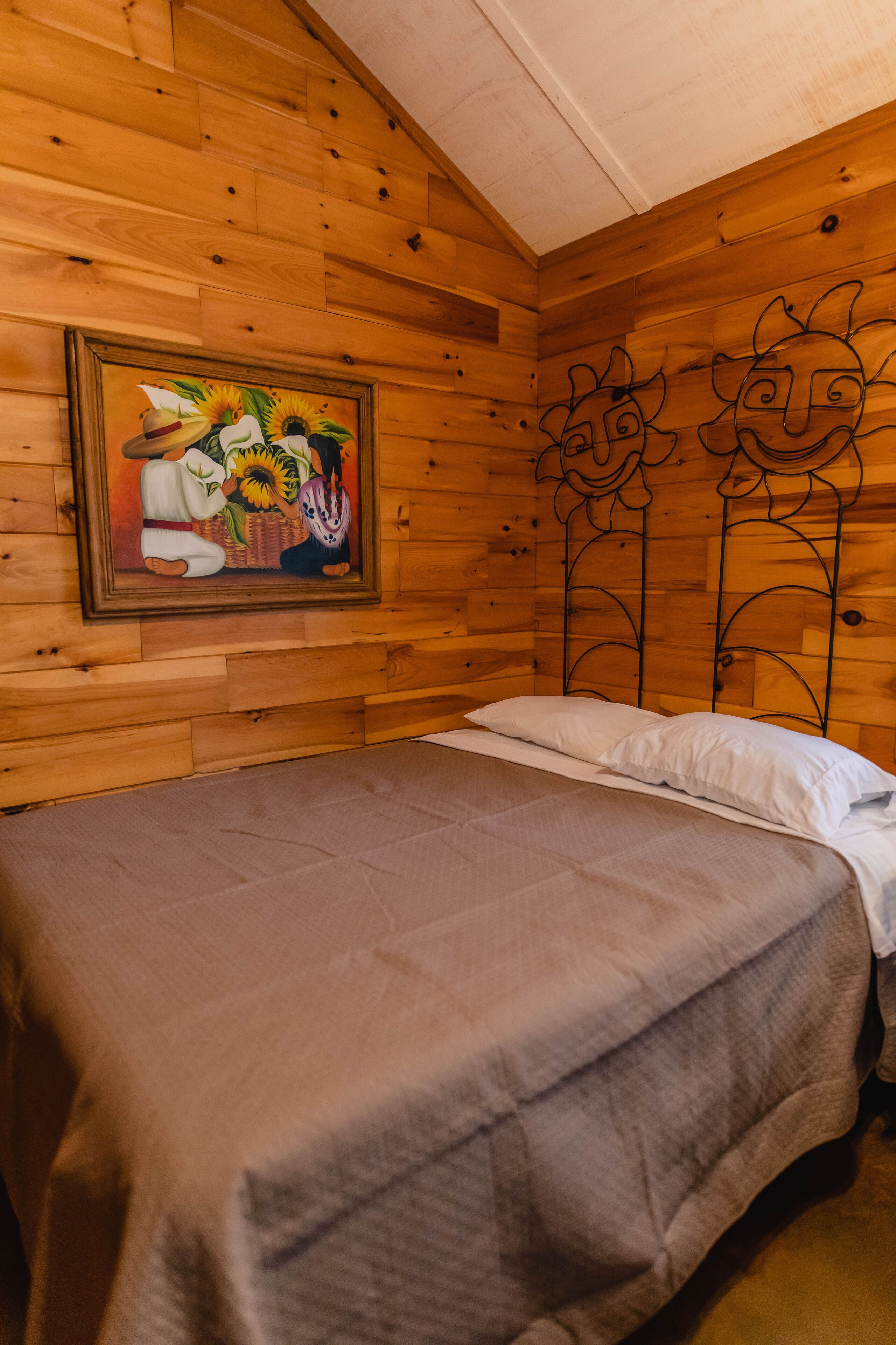 A wooden cabin room with a bed, a painting of sunflowers, and a metal headboard.
