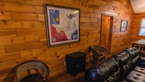 Interior de una cabaña de madera con un mapa enmarcado, un sofá de cuero y sillones de mimbre.