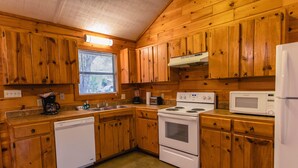 Una cocina con gabinetes de madera, lavavajillas, estufa, microondas y una ventana con persianas.