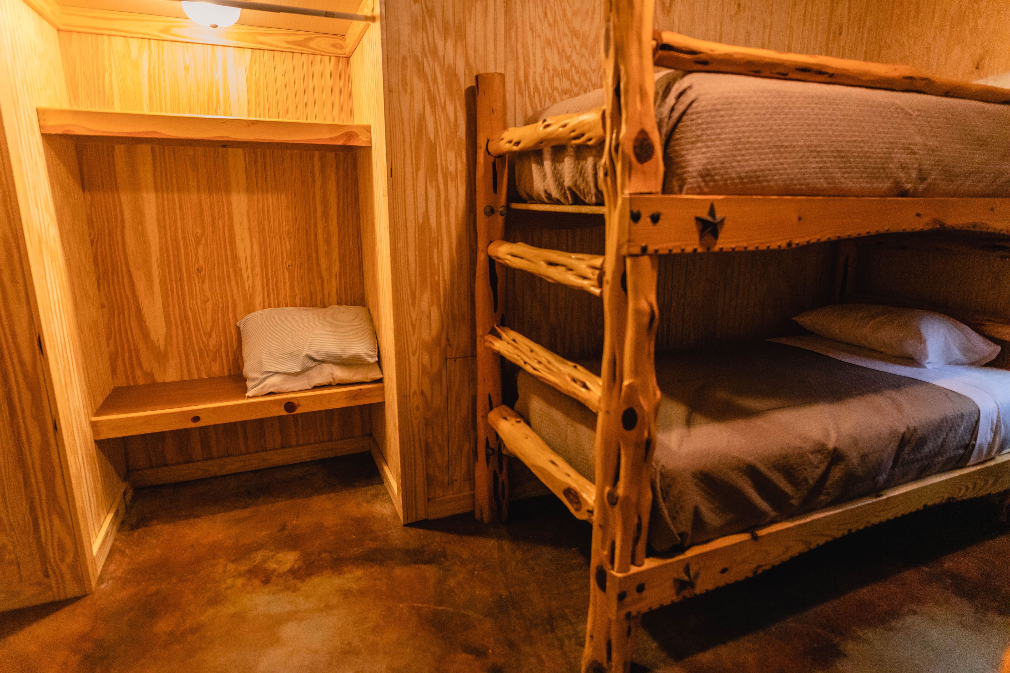 Una cama litera de madera con un estante encima, un banco y una mesita.