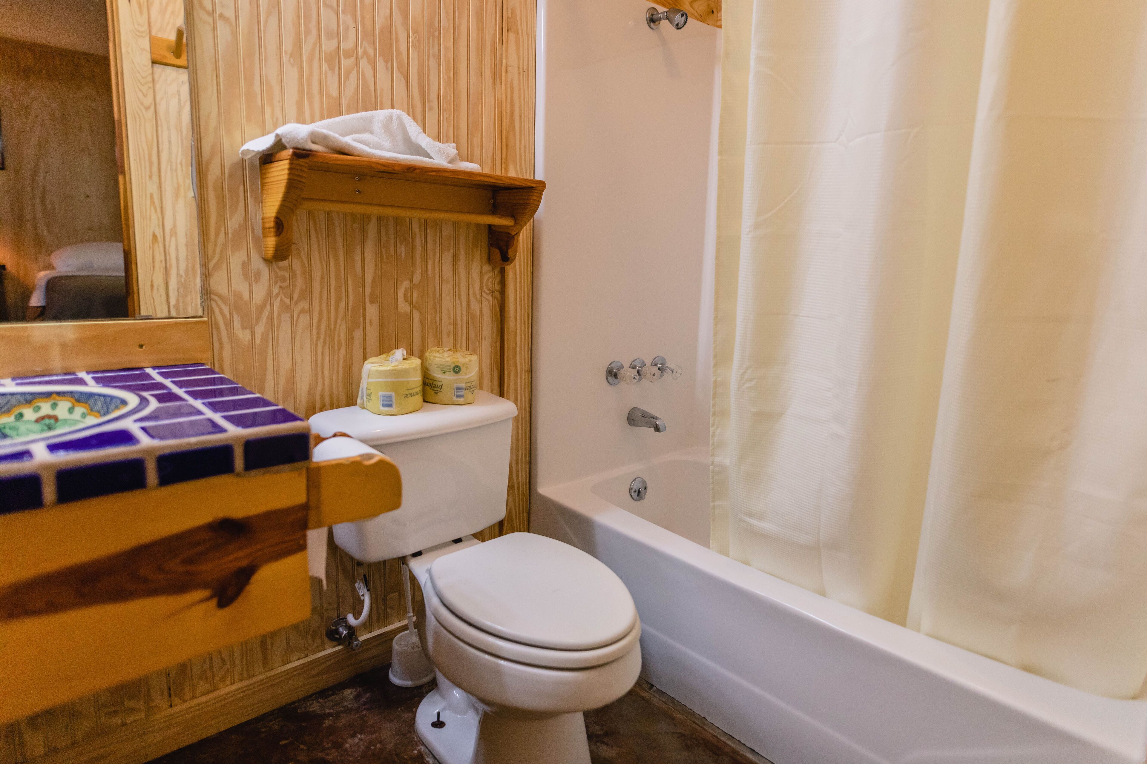 A bathroom with a wooden vanity, a toilet, a bathtub, and a shower curtain.