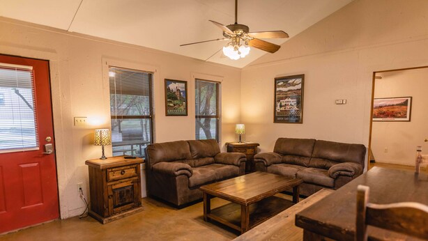 A living room with a red door, two brown leather sofas, a wooden coffee table, and a ceiling fan. - Frio Country Resort - Within walking distance to the Frio River! (Concan)