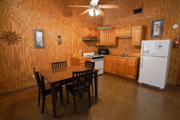 A kitchen with wooden cabinets, a white refrigerator, a stove, and a ceiling fan. - Frio Country Resort - Within walking distance to the Frio River! (Concan)