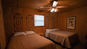 A room with two beds, wooden walls, a ceiling fan, and a window with blinds. - Frio Country Resort - Within walking distance to the Frio River! (Concan)
