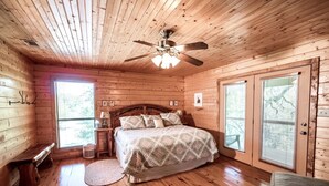Ein gemütliches Schlafzimmer einer Holzhütte mit einem Bett, einem Nachttisch, einer Lampe und einem Deckenventilator.