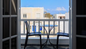 An open balcony with a checkered floor, two chairs, and a view of buildings and a blue sky.