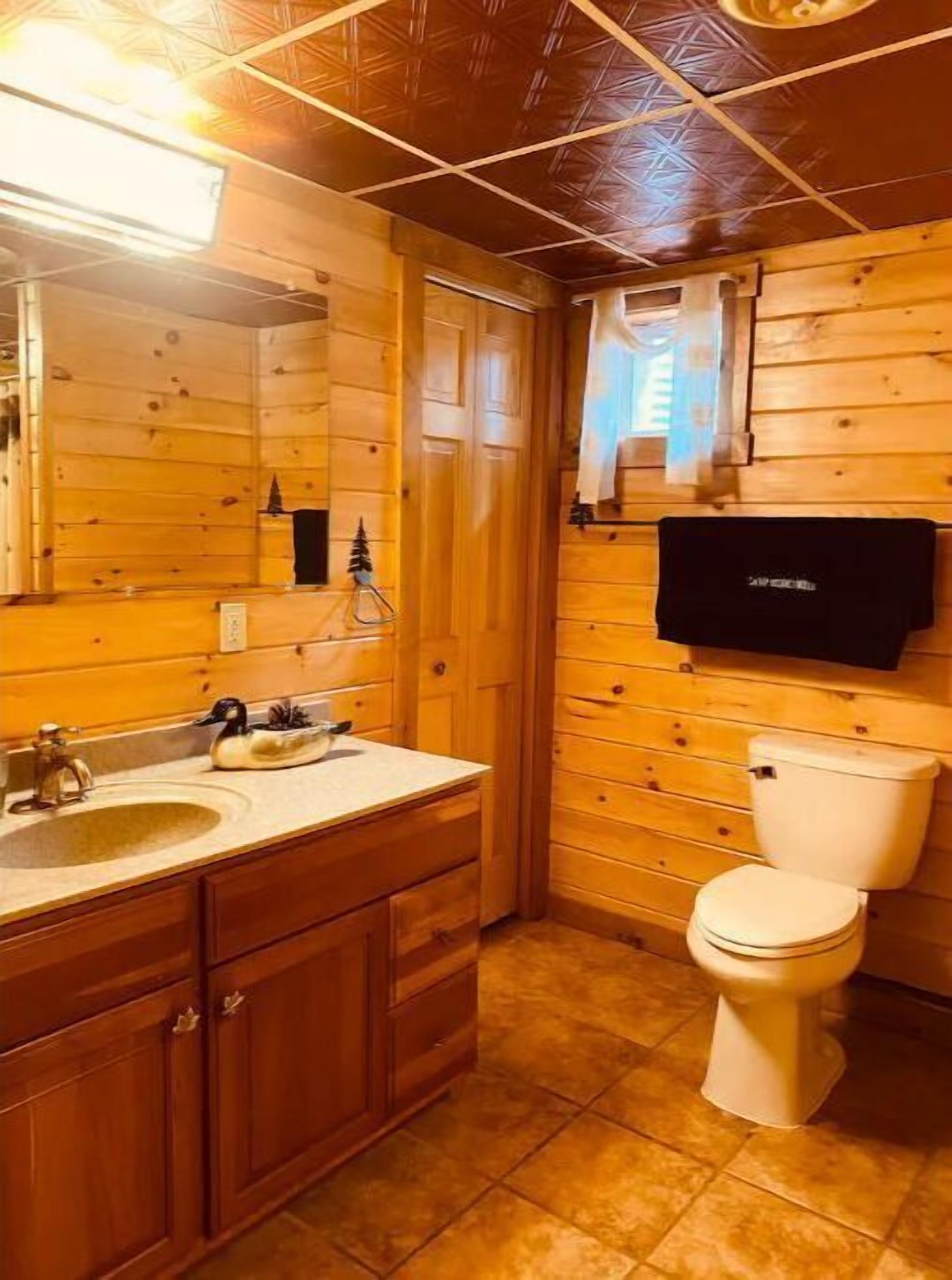 Een houten badkamer met een wastafel, spiegel en toilet.