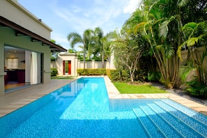 A swimming pool with a tiled edge, surrounded by a well-maintained lawn and palm trees.