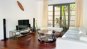 A modern living room with a flat-screen TV, a glass coffee table, a white sofa, and a large window with curtains. - Luxe 2br Pool Villa Walk to Bangtao Beach (Choeng Thale)