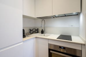 A modern kitchen with white cabinets, a stainless steel range hood, a built-in oven, and a digital clock.