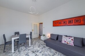 Una sala de estar moderna con comedor, suelo de piedra, un sofá gris y una obra de arte roja en la pared.