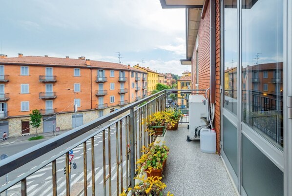 A balcony with a view of a street lined with colorful buildings, a metal railing, and potted plants.