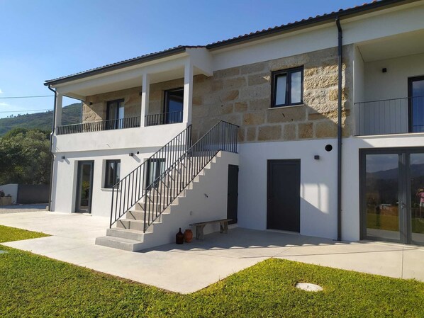 Uma casa de dois andares com varanda, escadaria e uma grande porta de vidro.