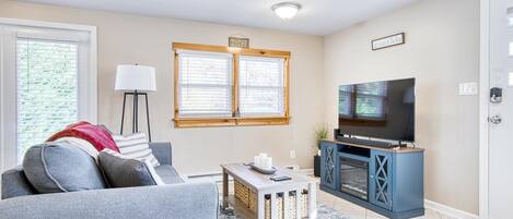 A living room with a grey sofa, a coffee table, a TV on a blue cabinet, and a window with blinds.