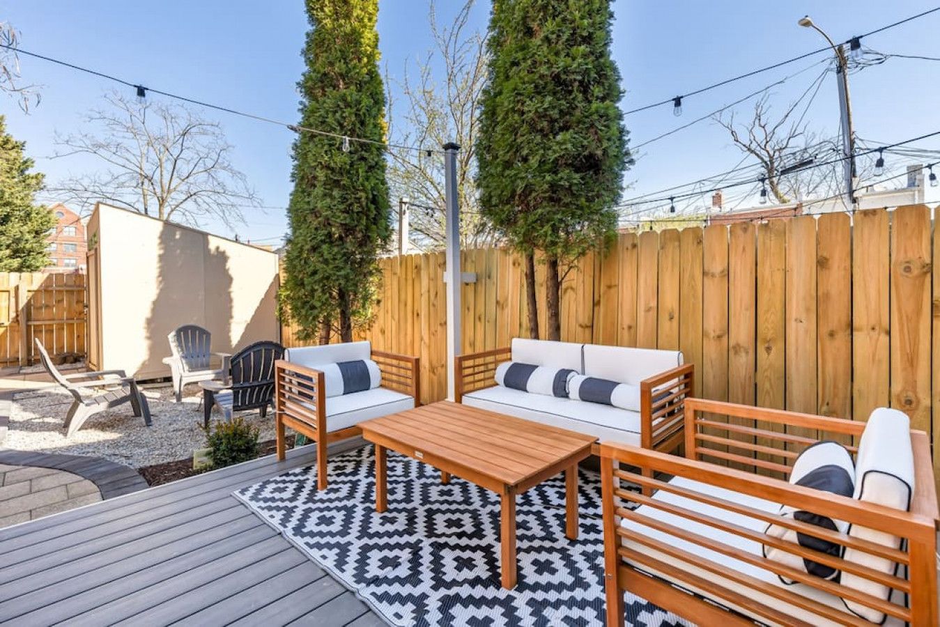 An outdoor patio area with a wooden deck, a patterned rug, a wooden table, and two sofas with cushions.