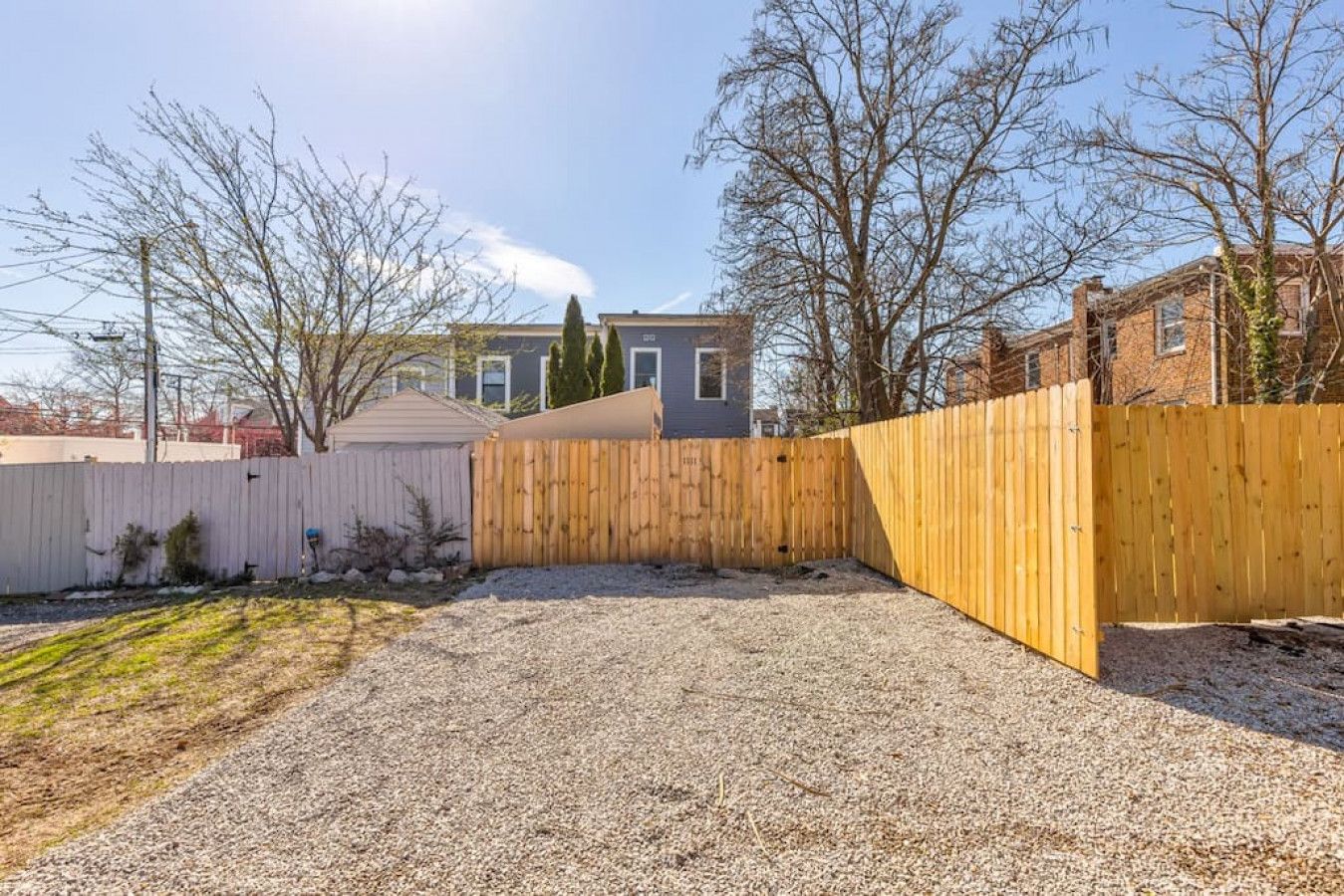 Un jardin avec une zone recouverte de gravier, une clôture en bois et une maison en arrière-plan.