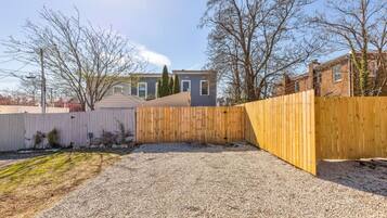 Un jardin avec une zone recouverte de gravier, une clôture en bois et une maison en arrière-plan.