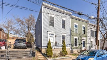 A two-story residential building with a front yard, a parked car, and a fence.
