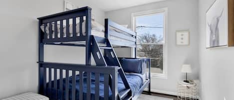 A bunk bed room with a window, a bedside table, and a lamp.