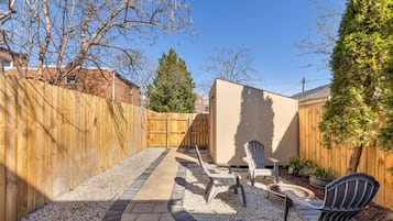A backyard with a wooden fence, a concrete patio, and outdoor seating.