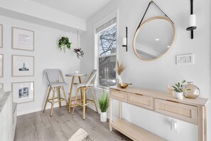 A modern interior with a dining area featuring wicker chairs and a round table, a console table with decorative items, and framed pictures on the wall.