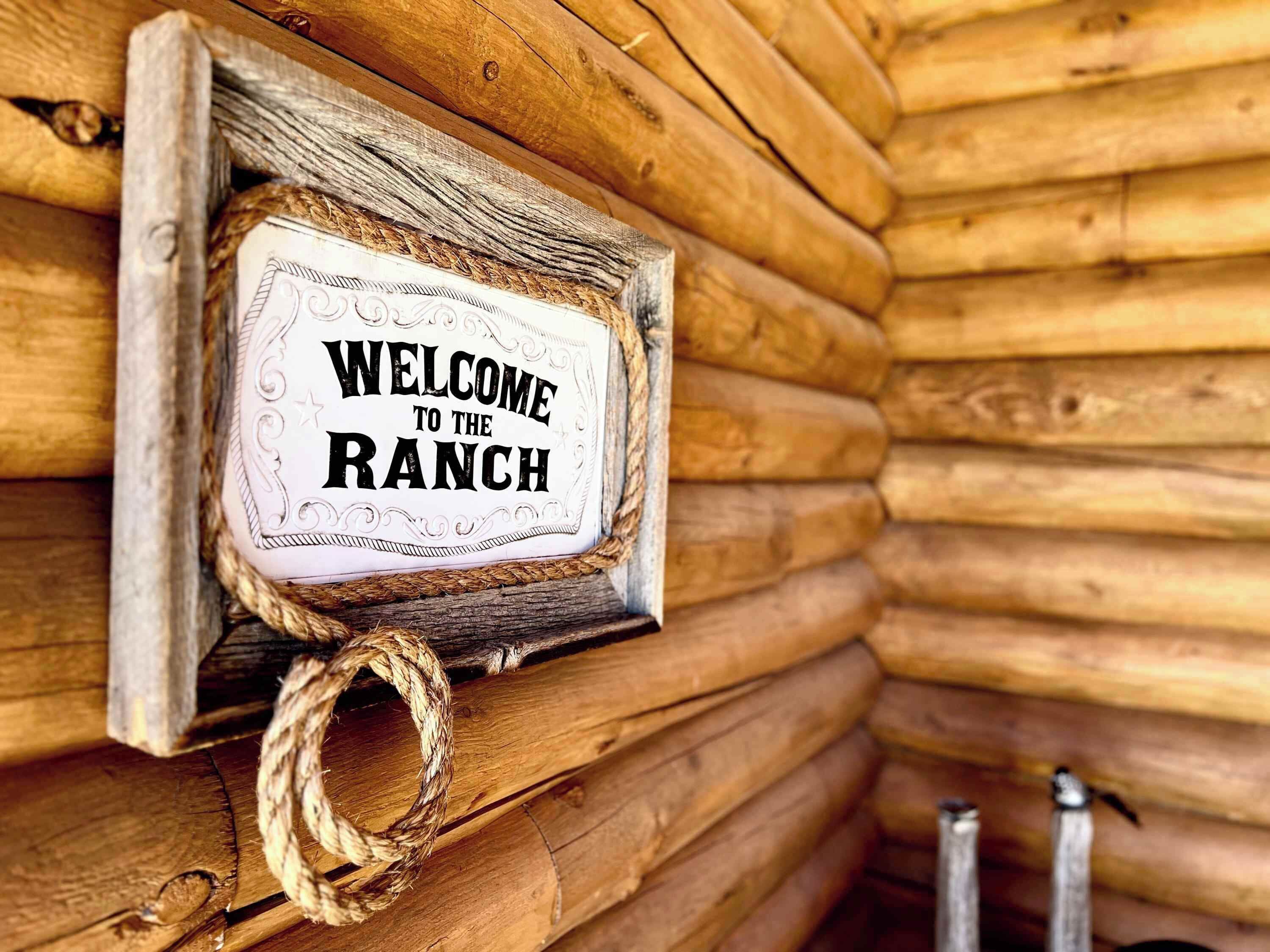 Una cabaña de madera con un letrero que dice 'BIENVENIDOS AL RANCH'.