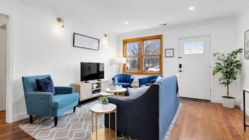 A modern living room with a blue sofa, a blue armchair, a television, and a small round table.